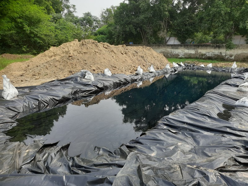 A large rectangle shaped pond lined with black waterproof material, with a large mound of earth next to it